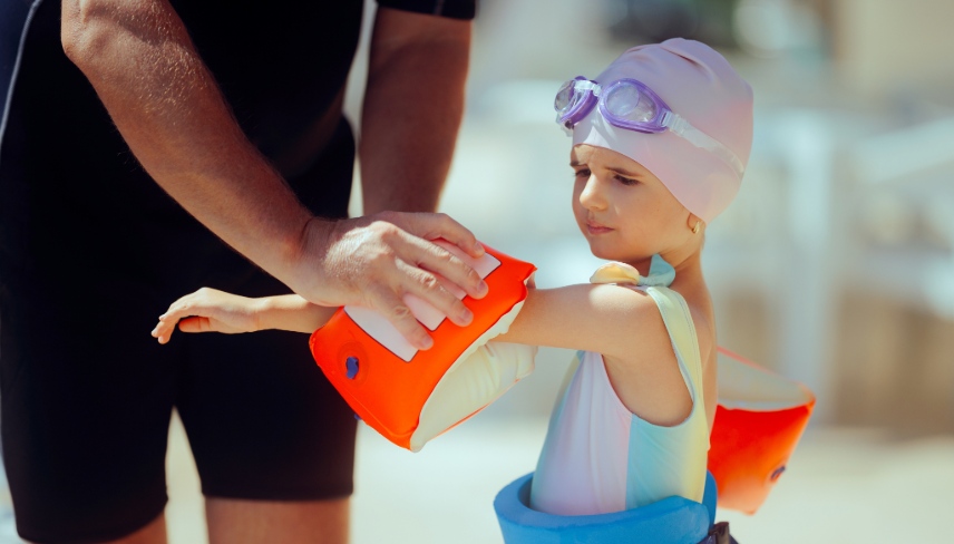  Swimming Instructor Helps Student Put on Inflatable Arm Floaties Little child wearing protective gear for her swimming lesson in the pool