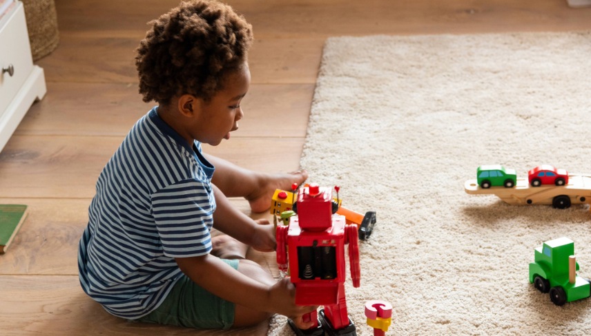 Child playing with toy robots and cars on a carpeted floor.