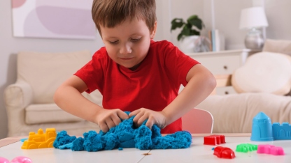Cute little boy playing with bright kinetic sand at table in room