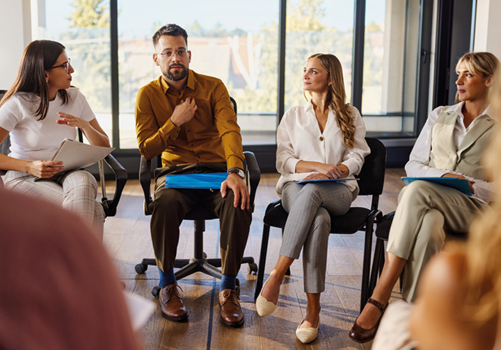 A group of people sat talking in a circle in a work setting. 