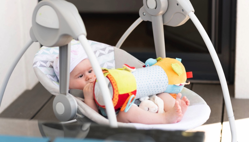 Close up of little 6 months old sweet baby girl in electric swing or cradle outdoors on sunny summer day. Infant background